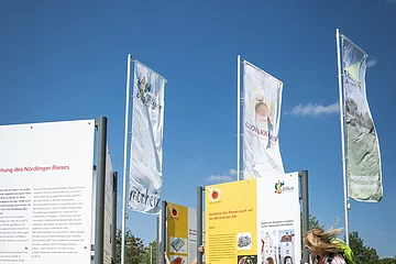 Infostelle Geopark Ries bei Monheim Ein Kind und eine Frau betrachten Informationstafeln im Freien, umgeben von Fahnen.
