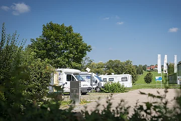 Wohnmobilstellplatz Monheim Wohnmobile parken auf einem Stellplatz, umgeben von Bäumen und Wiesen unter blauem Himmel.