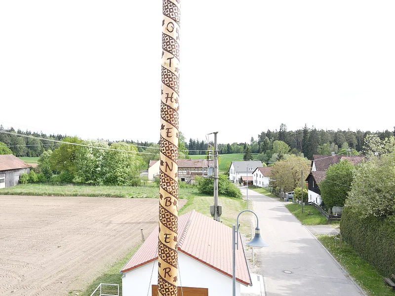 Maibaum 2026 Rothenberg Maibaum mit spiralförmiger Schrift in einem Dorf mit Häusern, Straße und Feldern im Hintergrund. Maibaum 2026 Rothenberg