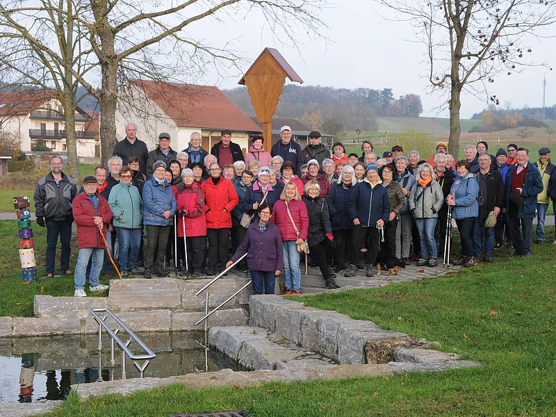 SoMit Wanderung 12.11.2025 in Wolferstadt Große Gruppe älterer Menschen steht im Park vor einem kleinen Wasserbecken mit Treppe und Geländer. Monatliche Wanderung für Senioren vom Verein Soziales Miteinander