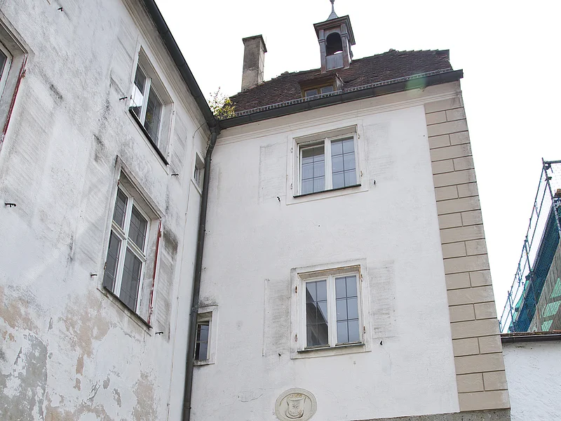 Historisches Stadttor mit Durchfahrt entlang einer Kopfsteinpflasterstraße. Das Tor und das Gebäude links daneben mit einer weiß verputzten Fassade und Verkehrsschildern rechts am Torbogen. Vor dem Tor ein kleines bepflanztes Beet.