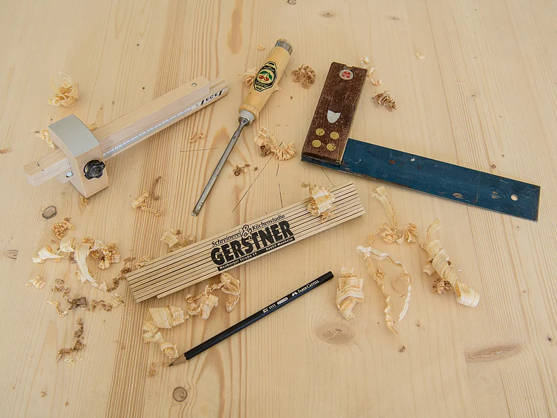 Schreinerei & Küchenstudio Gerstner - Werkzeug Holzwerkzeuge, Bleistift und Zollstock auf Holzplatte mit Holzspänen verteilt.