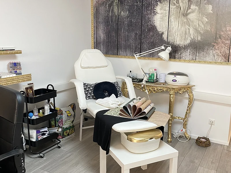 Behandlungsraum mit weißem Stuhl, Rollwagen, goldfarbenem Tisch und großem Blumenbild an der Wand.