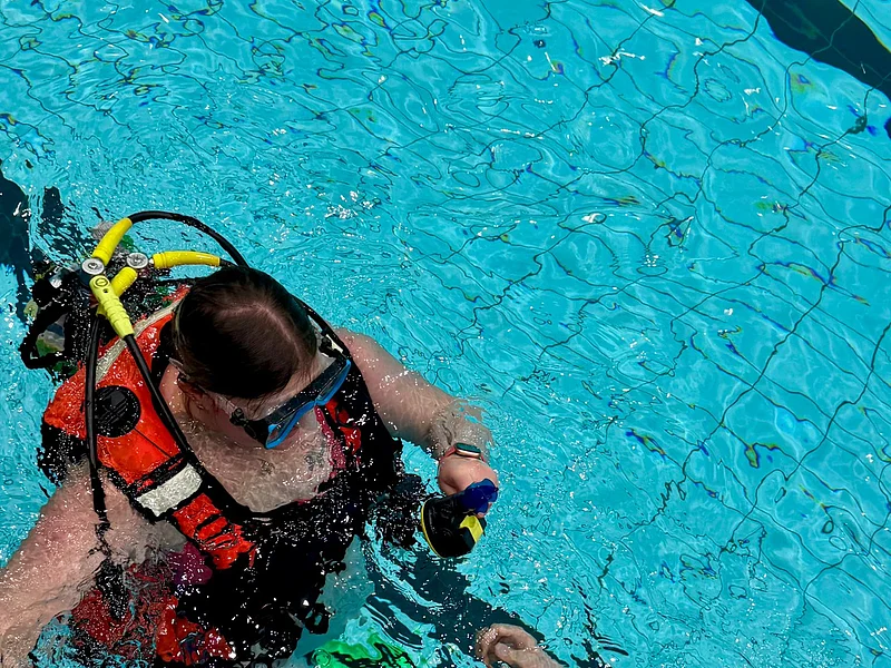 Zwei Personen mit Tauchausrüstung und Schwimmbrillen im Schwimmbecken, eine hält die Hand der anderen.