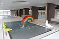 Innenansicht eines Schwimmbads, dem Jurabad Monheim, mit Kinderbecken, Regenbogenrutsche und Wasserspielzeugen. Im Hintergrund ein weiteres Schwimmbecken und ein großes offenes Fenster.