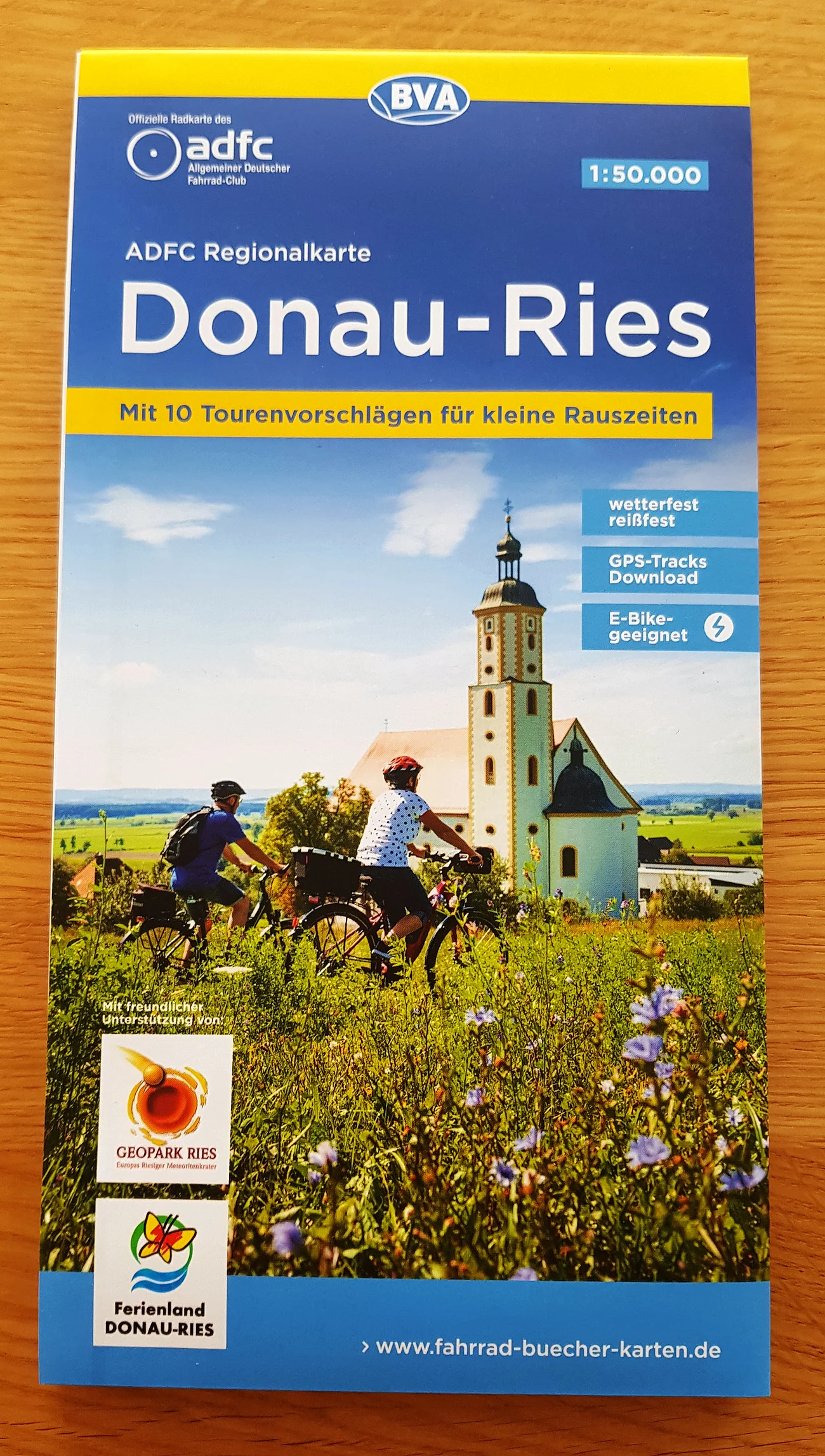 Cover der ADFC Regionalkarte Donau-Ries mit Radfahrern vor Kirche und Landschaft im Hintergrund. Unten links im Bild Logos vom Ferienland Donauries und des Geopark Ries.