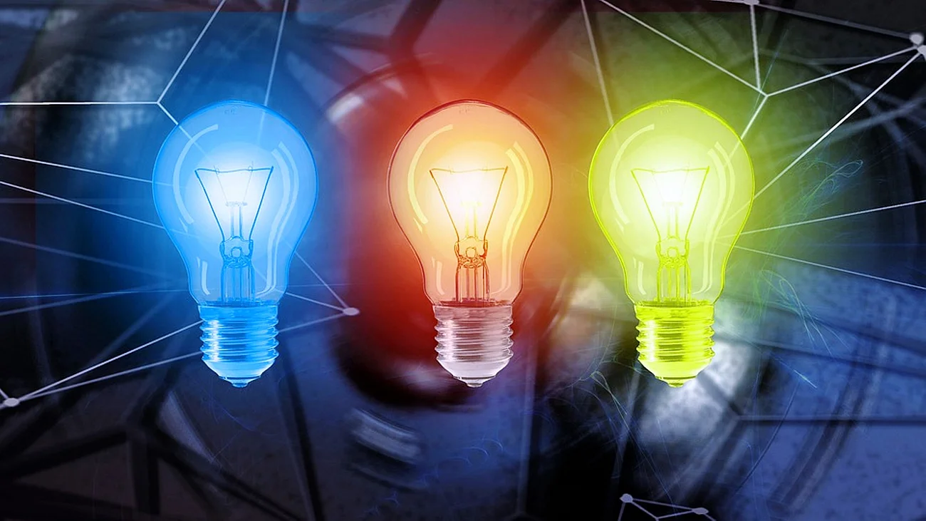 Energie-Versorgung Drei Glühbirnen nebeneinander in Blau, Rot und Gelb leuchten vor einem dunkelblauen Hintergrund mit Linien.