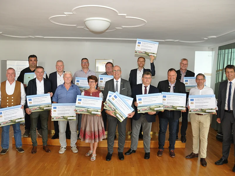 ELER-Förderung: Gruppenbild der dreizehn Kommunen und deren Vertretern, die in Schwaben mit 9,3 Millionen Euro gefördert werden. Gruppenfoto von 15 Personen in einem Raum, die große Förderbescheide in den Händen halten.