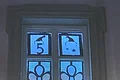 Adventskalenderfenster 05.12.2024 - Bürgermeister Adventskalenderfenster weihnachtlich dekoriert und von hinten beleuchtet mit zwei Engeldarstellungen, eine mit gelbem Stern, eine mit rotem Herz in der Körpermitte. Links oben im Eck Zahl 5 und rechts davon sind Sterne, beides mit einer Weihnachtsmütze darüber.