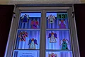 Adventskalenderfenster 13.12.2024 - Kinderchor Liederkranz Beleuchtetes Adventskalenderfenster mit zehn bunten Engel-Bastelarbeiten und darunter zwei Zettel mit Weihnachtsgrußtexten. Oben rechts im Eck die Zahl 13 auf Papier.