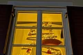Adventskalenderfenster 16.12.2024 - Wasserwacht Adventskalenderfenster mit weißem Rahmen und geöffneten roten Fensterläden weihnachtlich dekoriert. Darin Weihnachtsdeko wie ein Tannenbaum aus Holz mit einer Lichterkette, der mit Figuren wie Weihnachtsmänner, Leuchtturm und Engeln dekoriert ist. Rechts unten auf dem Fensterbrett steht ein Lebkuchenmann. Hinter dem Lebkuchenmann ist ein rot-weißer Rettungsring innen sichtbar.