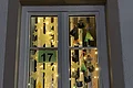 Adventskalenderfenster 18.12.2024 - Waldkindergarten Adventskalenderfenster mit einer Umrandung in beige weihnachtlich dekoriert. Darin von oben hängend gebastelte Weihnachtsdeko wie Papiersterne, Kerzen, Tannenbäume und Tiergesichter. In der Mitte des Fensters die Zahl 17 auf grünem Hintergrund. Das Fenster ist mit einer Lichterkette beleuchtet.