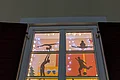 Adventskalenderfenster 04.12.2024 - TSV Adventskalenderfenster mit weißem Rahmen und roten Fensterläden weihnachtlich dekoriert. Darin fünf unterschiedliche Silhouetten von Sportlern beim Sport und links unten im Eck der Text „Frohe Weihnachten und ein gutes neues Jahr“ mit dem TSV Monheim Logo rechts daneben. Um das komplette Fenster eine leuchtende Lichterkette.
