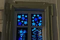 Adventskalenderfenster 24.12.2024 - Monheimer Ministranten Adventskalenderfenster weihnachtlich dekoriert auf schwarzem Hintergrund mit leuchtenden Sternen oben im Fenster, einem Weihnachtsbaum rechts im Fenster, Krippenfiguren links davon und dem Schriftzug "Die Monheimer Ministranten wünschen gesegnete Weihnachten." Unter dem Tannenbaum die Zahl 24. Alles in hell- und dunkelblau und von hinten beleuchtet.