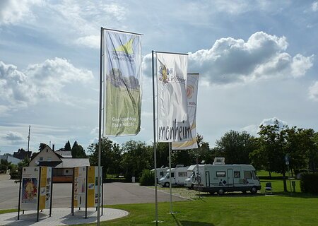 Die Geopark Infostelle mit Flaggen und im Hintergrund die Wohnmobile auf dem Wohnmobilstellplatz in Monheim