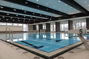 Das Monheimer Hallenbad, das Jurabad, mit gefülltem Schwimmbecken, Startblöcken und großen Fenstern, die Tageslicht hereinlassen.