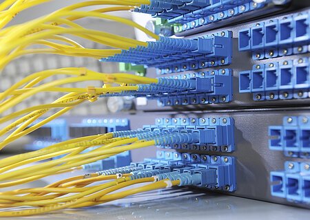 Gelbe Glasfaserkabel sind in blaue Anschlüsse eines Netzwerkservers eingesteckt.