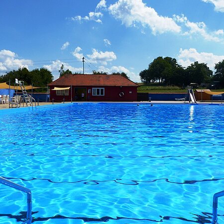 Das Freibad in Monheim: Schwimmbecken mit klarem Wasser, umgeben von Liegestühlen, einem roten Gebäude und Umkleidekabinen im Hintergrund.