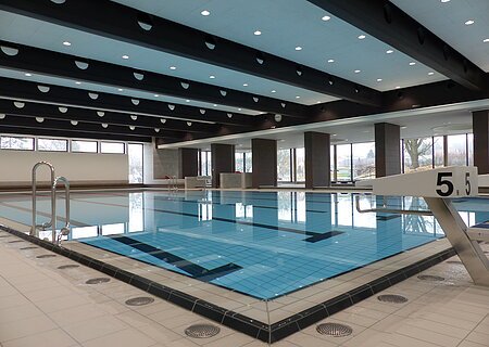Das Monheimer Hallenbad, das Jurabad, mit gefülltem Schwimmbecken, Startblöcken und großen Fenstern, die Tageslicht hereinlassen.