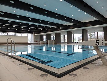 Das Monheimer Hallenbad, das Jurabad, mit gefülltem Schwimmbecken, Startblöcken und großen Fenstern, die Tageslicht hereinlassen.