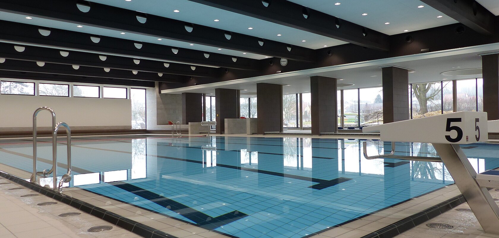 Das Monheimer Hallenbad, das Jurabad, mit gefülltem Schwimmbecken, Startblöcken und großen Fenstern, die Tageslicht hereinlassen.