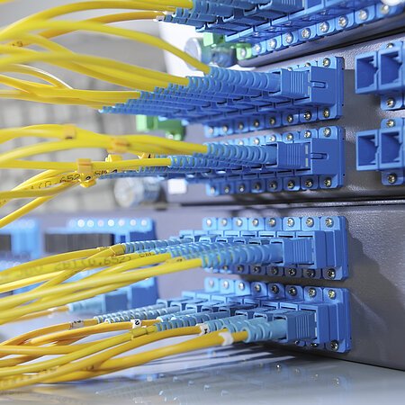 Gelbe Glasfaserkabel sind in blaue Anschlüsse eines Netzwerkservers eingesteckt.