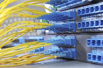 Breitbanderschließung Gelbe Glasfaserkabel sind in blaue Anschlüsse eines Netzwerkservers eingesteckt.