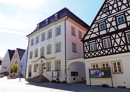 Straßenansicht der Monheimer Innenstadt: Im Vordergrund das Rathaus der Stadt Monheim, mit weiteren mehreren Gebäuden, darunter ein Fachwerkhaus, das man Schindlerhaus nennt.