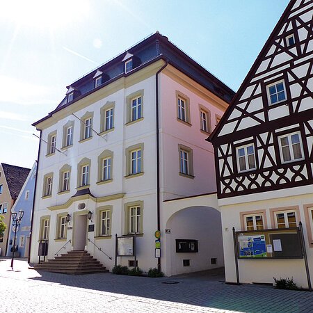 Straßenansicht der Monheimer Innenstadt: Im Vordergrund das Rathaus der Stadt Monheim, mit weiteren mehreren Gebäuden, darunter ein Fachwerkhaus, das man Schindlerhaus nennt.