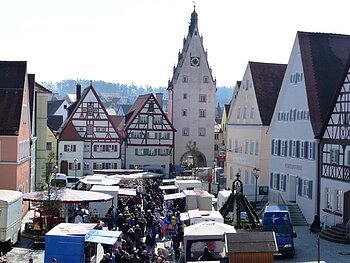 Herzlich Willkommen beim Josefsmarkt in Monheim Josefsmarkt in Monheim in der Altstadt: auf dem Marktplatz entlang Fachwerkhäuser, ein Turm mit Uhr und Menschenmengen zwischen vielen Marktständen bei Tageslicht.