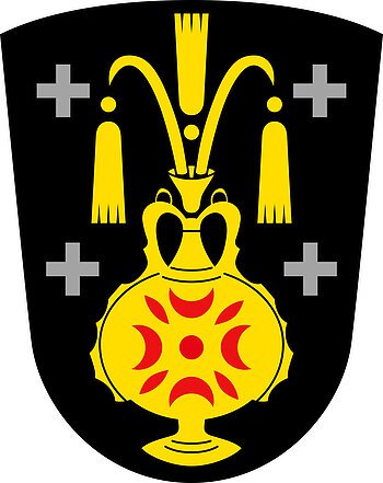 Das Wappen des Monheimer Stadtteils Kölburg: gelber Krug auf schwarzem Hintergrund, auf dem Krug rote Muster. Jeweils links und rechts zwei graue Kreuze.