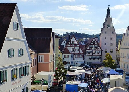 Menschenmenge auf dem belebten Monheimer Marktplatz mit historischen Gebäuden und vielen Verkaufsständen bei sonnigem Wetter.