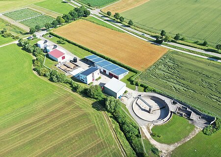 Luftaufnahme der städtische Kläranlage Monheim mit Solarpaneelen auf den Dächern, umgeben von grünen Feldern und Straßen.
