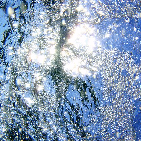 Lichtreflexionen und Luftblasen unter Wasser, mit blauem Himmel über dem Wasser.
