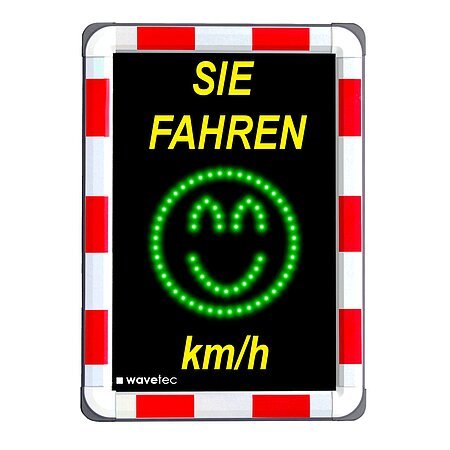Bild eines Geschwindigkeitsmessgeräts im Straßenverkehr, darauf oben gelber Text "Sie fahren" und unten "km/h". Dazwischen ein grünes Smiley-Gesicht aus LEDs. Der Rand außen ist rot/weiß.