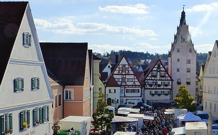 Menschenmenge auf dem belebten Monheimer Marktplatz mit historischen Gebäuden und vielen Verkaufsständen bei sonnigem Wetter.