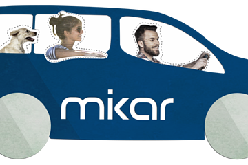 Blaues Auto mit zwei Personen und einem Hund, auf dem Auto der Schriftzug "mikar" auf der Seite. Fahrer hält das Lenkrad.