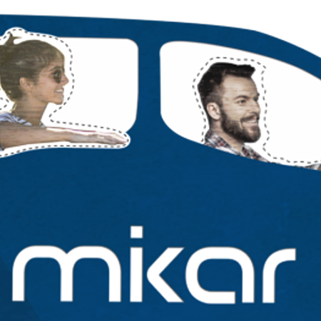 Blaues Auto mit zwei Personen und einem Hund, auf dem Auto der Schriftzug "mikar" auf der Seite. Fahrer hält das Lenkrad.