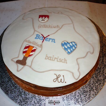 Torte mit einer Karte des Drei-Länder-Ecks, darauf Symbole und Schriftzüge für fränkisch, schwäbisch und bayerisch, auf einer silbernen Unterlage.