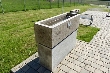 Armbecken der Kneipp Gesundheitsanlage in Monheim auf gepflastertem Weg neben einer Wiese, mit einem Wasserhahn an der Oberseite.