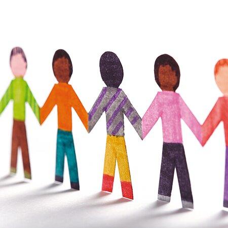 Papierfiguren, die Kinder symbolisieren in verschiedenen Farben halten sich an den Händen und bilden eine Kette.
