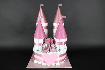 Windeltorte in Form eines Schlosses mit rosa Türmen und Babyschuhen auf schwarzem Hintergrund.