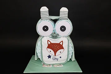 Windeltorte in Form einer Eule mit großen Augen, Socken und einem Lätzchen mit Fuchs und der Aufschrift "tiny" darauf.