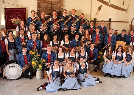 Gruppe von Menschen eines Musikvereins in traditioneller Kleidung mit Musikinstrumenten in einem Raum.