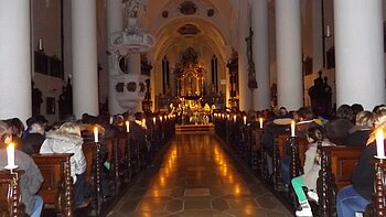 Adventskonzert in Monheim - besinnliche Stimmung in der Stadtpfarrkirche St. Walburga Innenraum einer Kirche mit Kerzen beleuchtet, Menschen sitzen auf Holzbänken, Blick auf den Altar im Hintergrund.