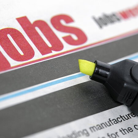 Zeitungsseite mit dem Wort "Jobs" in großen roten Buchstaben und ein gelber Textmarker liegt auf der Zeitung.