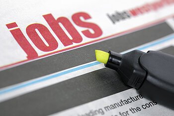 Zeitungsseite mit dem Wort "Jobs" in großen roten Buchstaben und ein gelber Textmarker liegt auf der Zeitung.
