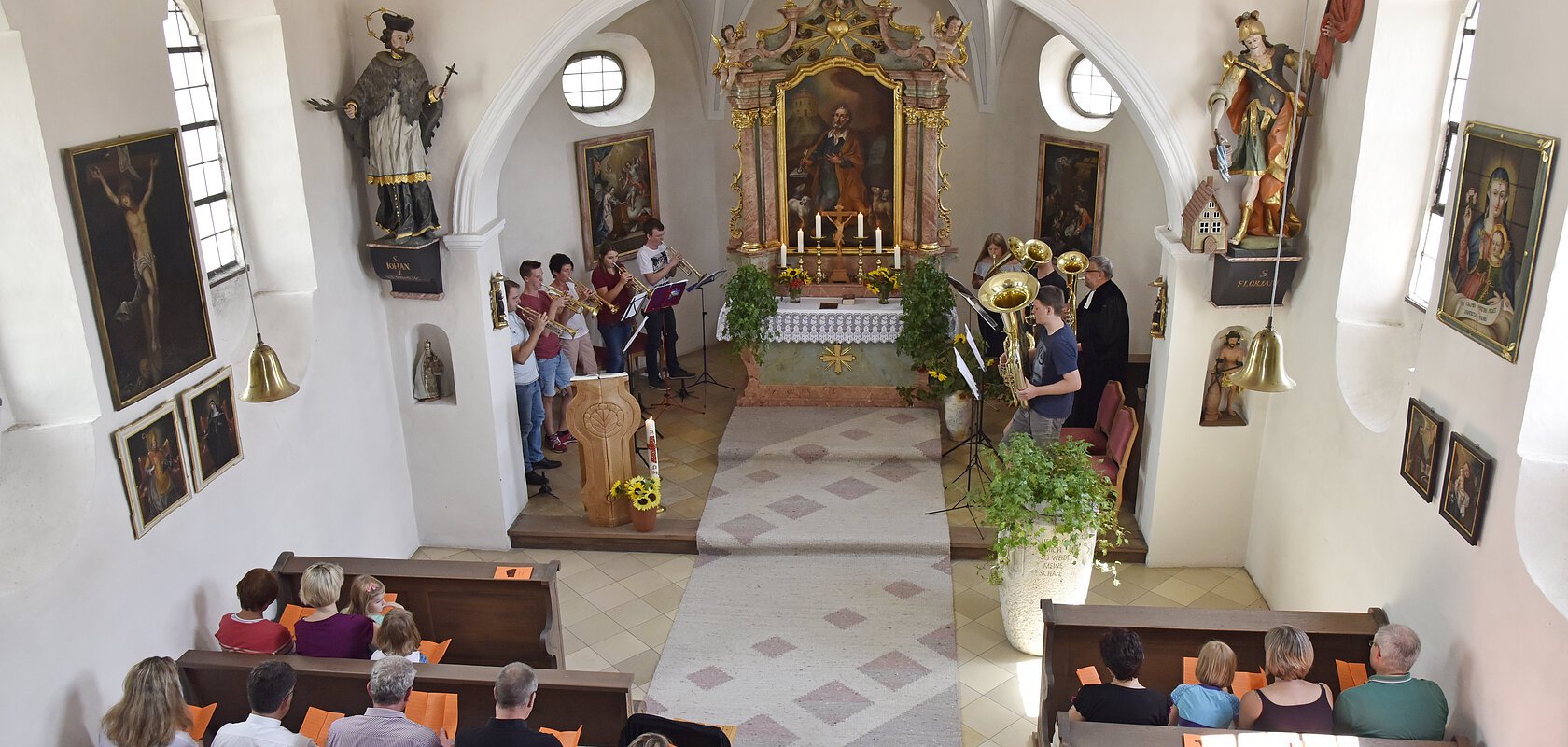 Innenansicht einer Kirche mit Menschen auf Bänken, Musiker spielen vorne Instrumente am Altar.