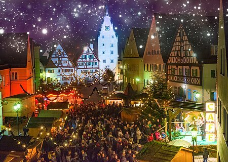 Abendaufnahme des Monheimer Weihnachtsmarktes in der Altstadt von Monheim: mit Fachwerkhäusern, Menschenmengen, Lichtern, Verkaufsständen und einer Bühne