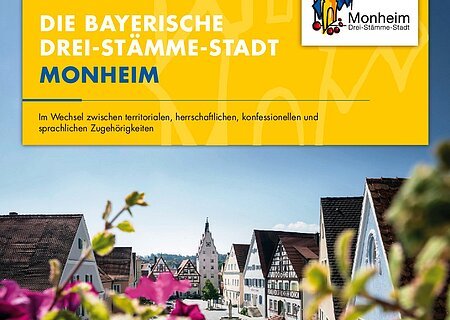 Vorstellung der bayerische "Drei-Stämme-Stadt" Monheim anhand eines Plakats. Auf dem Foto die Stadtansicht von Monheim mit Fachwerkhäusern, blauem Himmel und unscharfen blühenden pinken Blumen im Vordergrund. Oben auf gelbem Hintergrund der dazugehörige Text: "Die bayerische Drei-Stämme-Stadt Monheim". Rechts oben das Logo der Stadt Monheim.